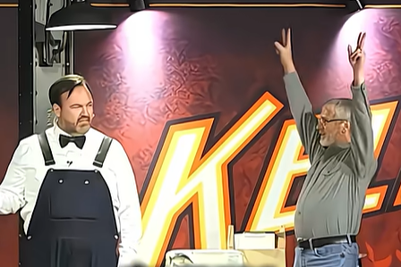 Matt Donnelly on stage with an audience member who exclaims something with his arms raised above his head